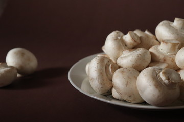 Fototapeta na wymiar raw mushrooms on a plate on dark brown background