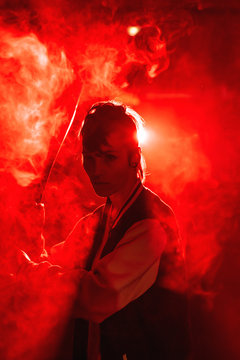 Rebel woman in casual jacket with piercing and modern hairstyle holding bat among colorful red light and steam