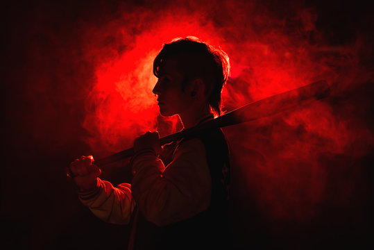 Rebel woman in casual jacket with piercing and modern hairstyle holding bat among colorful red light and steam