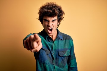 Young handsome man wearing casual shirt standing over isolated yellow background pointing displeased and frustrated to the camera, angry and furious with you