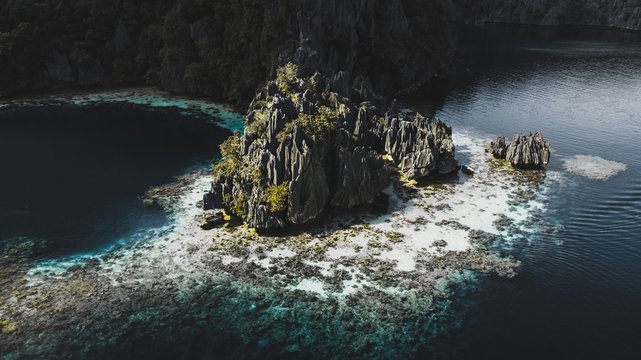 Aerial view of rough rocks on island with green plants among blue calm sea in Coron, Philippines