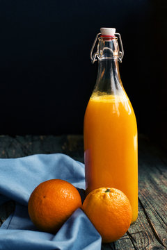 Bottle of fresh citric orange juice placed near fresh oranges on a wooden dark rustic table at dark background
