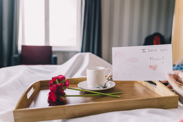 Coffee and breakfast prepared on a tray with a letter and flower as a gift for Mother's Day
