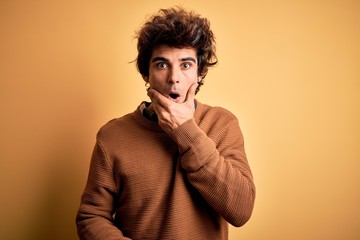 Young handsome man wearing casual shirt and sweater over isolated yellow background Looking fascinated with disbelief, surprise and amazed expression with hands on chin