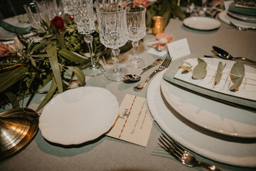Various dishware and name card arranged with flowers and elegant glassware on table for wedding reception