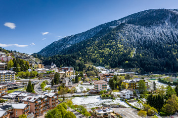 Fototapeta premium The Improbable aerial landscape of village Molveno, Italy, snow covered mountains Dolomites on background, roof tops of chalet, sunny weather