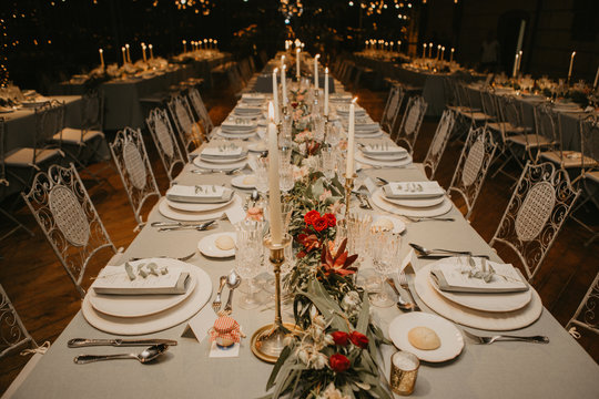 Candles and flowers placed near tableware old long table during wedding banquet in spacious room at night