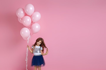 Smiling adorable little child girl posing with pastel pink air balloons isolated over pink background. Beautiful happy kid on a birthday party. copy space