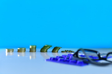 Economy crisis, Recession, Business crisis and Finance crisis concept background showing coins stacks, calculator and glasses over a blue backgorund 