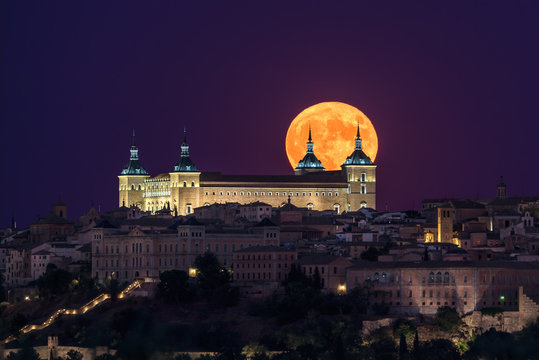Wonderful scenery of illuminated ancient palace built over town in colorful night with full red Moon in Toledo
