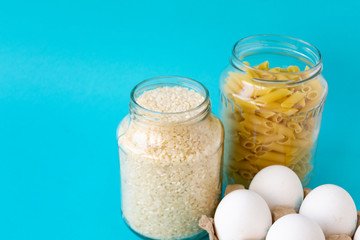 Noodles, rice, pasta in jars and eggs lie on a blue background. Raw food for cooking.