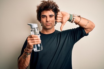 Young handsome man holding bottle of water standing over isolated white background with angry face,...