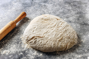 Dough and wooden rolling pin on a table strewn with flour.