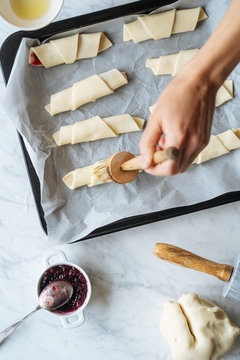 From above crop qualified cook carefully brushing tasty croissants on baking sheet on table in kitchen