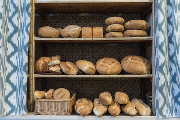 Loaves of assorted fresh bread for sale placed on shabby shelves near curtains in bakery