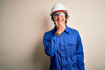 Young constructor man wearing uniform and security helmet over isolated white background looking confident at the camera smiling with crossed arms and hand raised on chin. Thinking positive.