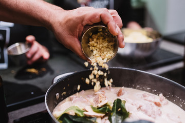 Crop chef spilling fresh ingredient into pan with stew while preparing dinner during cooking lesson in restaurant in Navarre, Spain