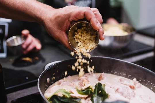 Crop chef spilling fresh ingredient into pan with stew while preparing dinner during cooking lesson in restaurant in Navarre, Spain