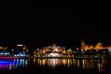 Fototapeta na wymiar Historic buildings at night. View across the Odra River in Szczecin. Lights of a passing ship