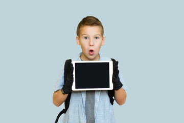 schoolboy boy of 10 years with a tablet backpack in medical gloves on an isolated light blue background, the topic of distance learning in a pandemic