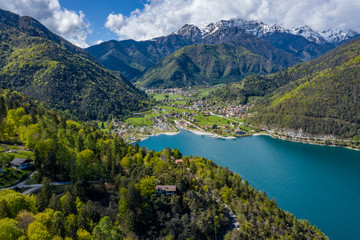 Fototapeta na wymiar The Improbable aerial landscape of village Molveno, Italy, azure water of lake, empty beach, snow covered mountains Dolomites on background, roof top of chalet, sunny weather, a piers, coastline, 