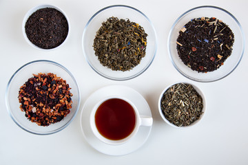 Assortment of dry tea in round bowls on a white background.