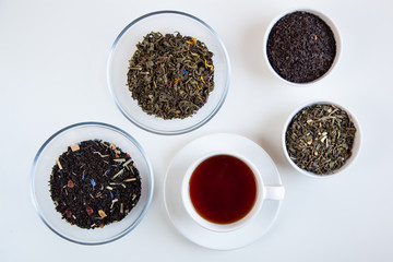 Assortment of dry tea in round bowls on a white background.