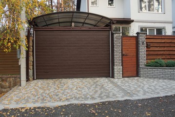 private garage with a brown closed gate and part of a wooden fence and a door on the sidewalk on a rural street