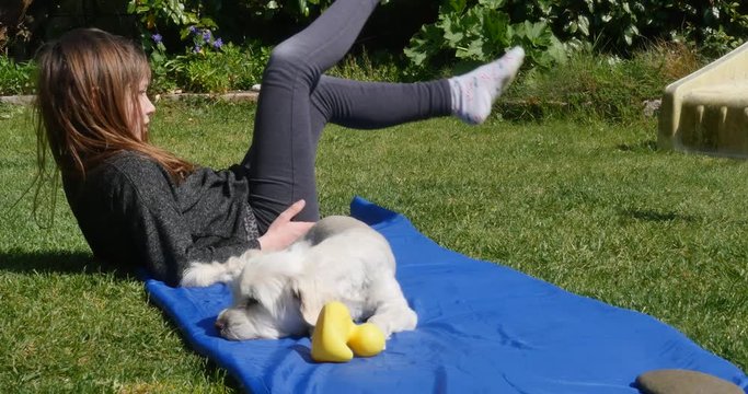 Pretty little girl doing physical exercises with her dog in the garden