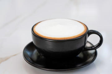 Hot cappuccino coffee with white cream foam serve in black coffee cup set, lay on marble table,