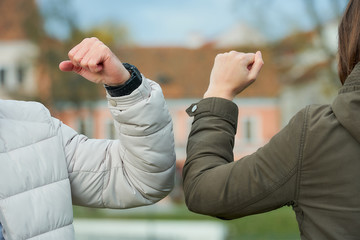 A close-up photo of elbow bumping. Elbow greeting to avoid the spread of coronavirus (COVID-19). Friends in medical face masks going to bump elbows instead of greeting with hug or handshake.