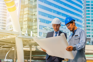 Engineer and worker with helmet looking paper plans at construct