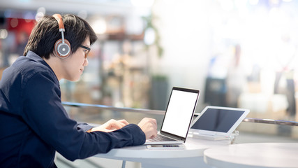 Asian businessman wearing headphones listening to music while working with laptop computer at home office. Male office worker searching information on internet platform. Work from anywhere concept