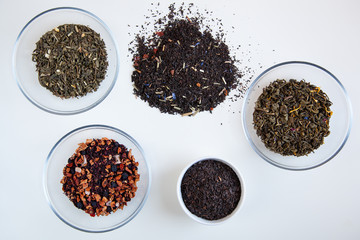 Assortment of dry tea in round bowls on a white background.