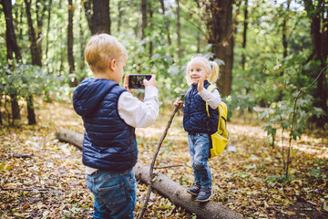 Children preschoolers Caucasian brother and sister take pictures of each other on mobile phone camera in forest park autumn. theme of hobby and active lifestyle for child. Profession photographer