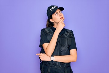 Young police woman wearing security bulletproof vest uniform over purple background with hand on chin thinking about question, pensive expression. Smiling with thoughtful face. Doubt concept.