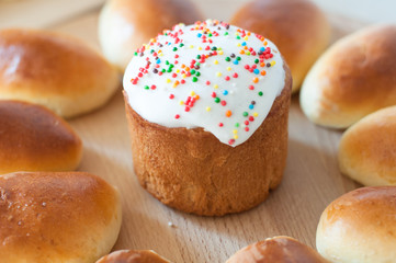 homemade easter cake with white sugar glaze and color sprinkle near patties on wooden board