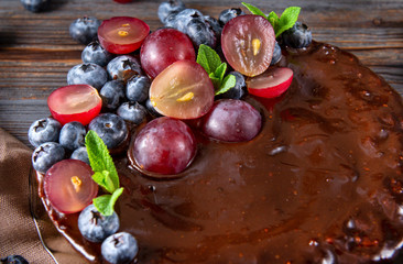 chocolate cake with fresh blueberries, red grapes and mint on a dark brown wooden background, pie, top view