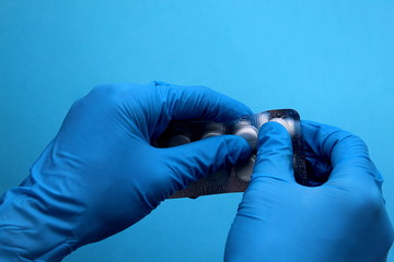 Hands in blue medical gloves squeeze a pill out of the package