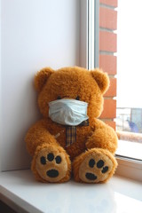 On the windowsill sits a toy bear in a medical mask and with a thermometer