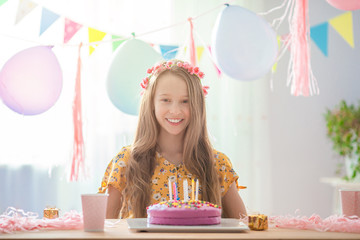 Caucasian girl is dreamily smiling and looking at birthday rainbow cake. Festive colorful...
