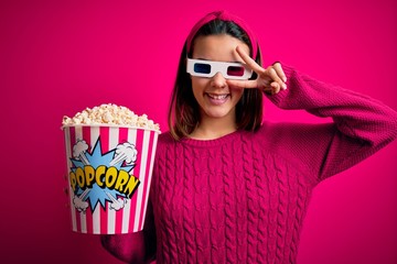 Obraz premium Young beautiful girl watching movie using 3d glasses eating box with popcorns Doing peace symbol with fingers over face, smiling cheerful showing victory