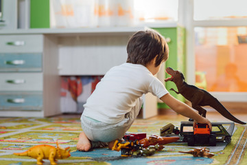 Adorable toddler playing with dinosaurs around lots of toys at home. Stay home.