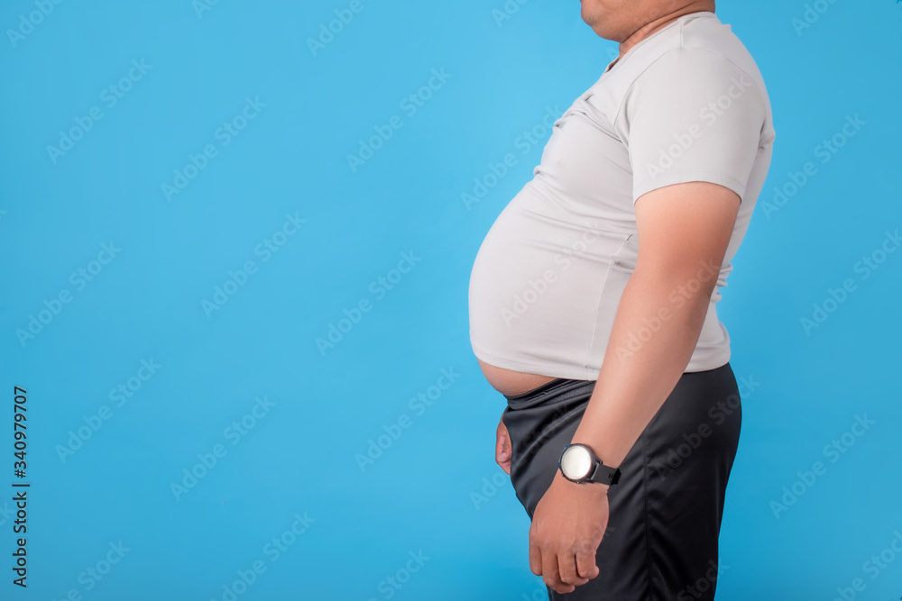 Wall mural fat man showing his belly on a blue background in the studio