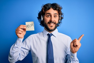 Young handsome call center agent man with beard working using headset holding help reminder very happy pointing with hand and finger to the side