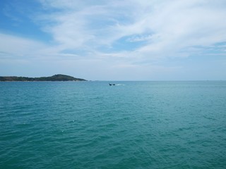 Panoramic view with sea expanse, island on the horizon, small moving longtail boat in a distance, beautiful sky with white clouds. Seascape and open ocean. Calm surface of azure clear water. Panorama.