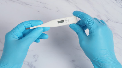 Digital thermometer white color in doctor hands wearing hospital medical gloves light blue color which can shown checking temperature numbers in celsius or fahrenheit degree for pandemic fever
