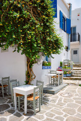 Fototapeta na wymiar Picturesque narrow street with traditional whitewashed houses with cafe tables of Naousa town in famous tourist attraction Paros island, Greece