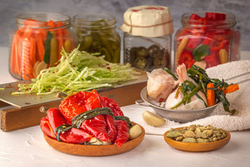 Fermented red hot peppers to enhance immunity with spices and radish grated on a hand grater on a light wooden table against a background of glass jars with pickled products