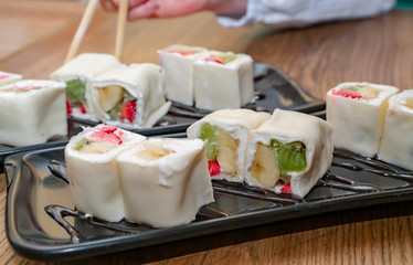 Sweet dessert rolls minari from strawberry, kiwi, banana and cream cheese wrapped in rice pastry is real dianty. Various fruits and berries inside, pancake outside, served on stylish black plates.